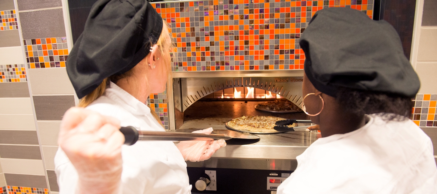 Students placing pizza in the pizza oven